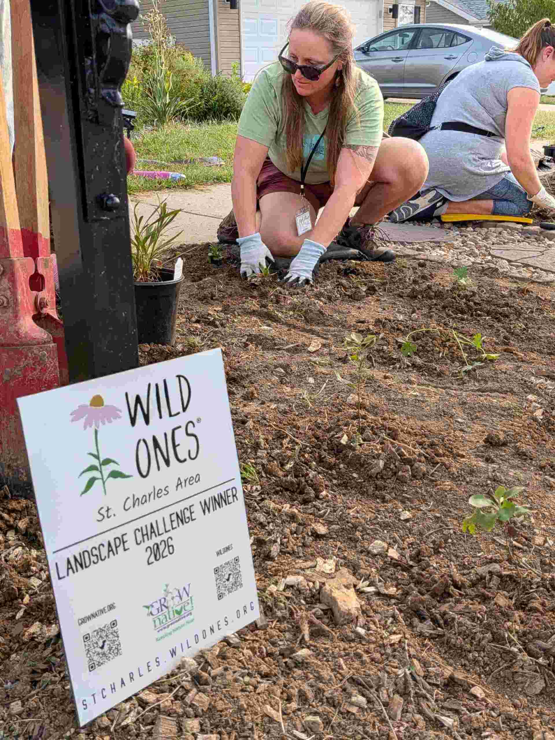 A small sign noting this area is from the Landscape Challenge sits in front of the mailbox while members pat down dirt around the installed plants